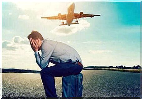 A man sitting on his suitcase in front of a plane taking off. 